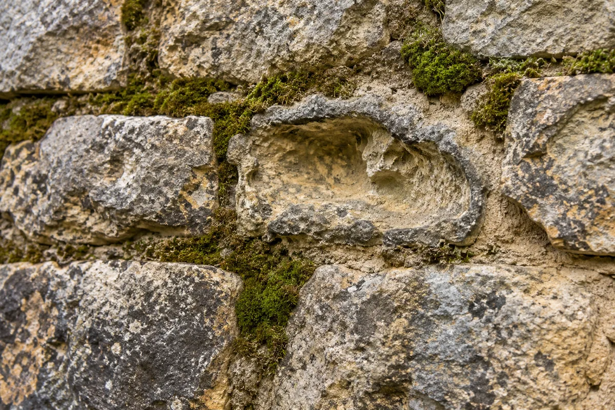Joints creusés et sableux colonisés par la mousse sur un mur de moellons calcaires, autour d&rsquo;une pierre érodée près d&rsquo;un ancien joint gris