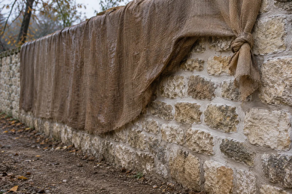 Toile de jute humide protégeant un mur de moellons calcaires fraîchement rejointoyé à la chaux